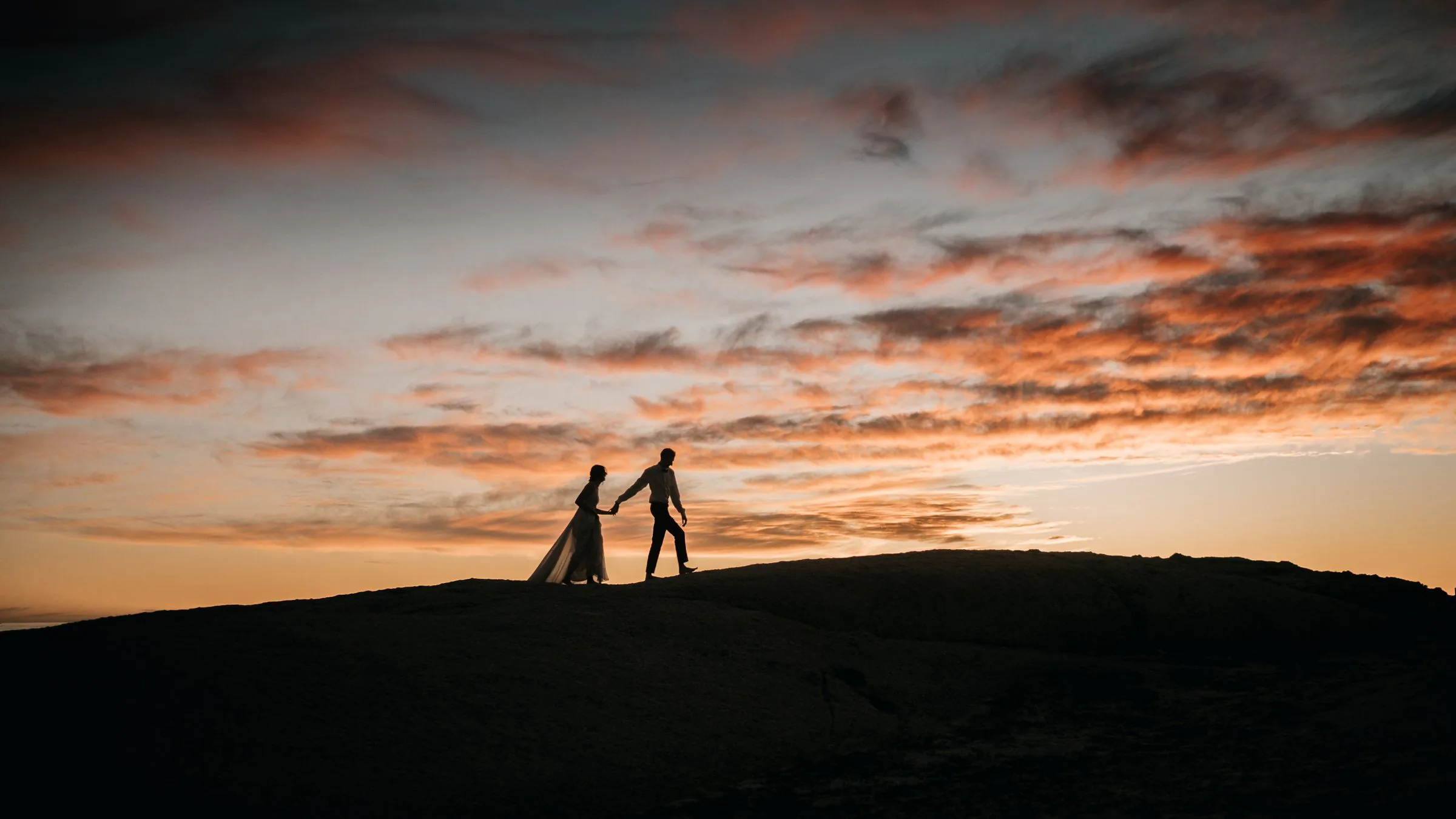 Des mariés en silhouette marchent main dans la main au coucher du soleil