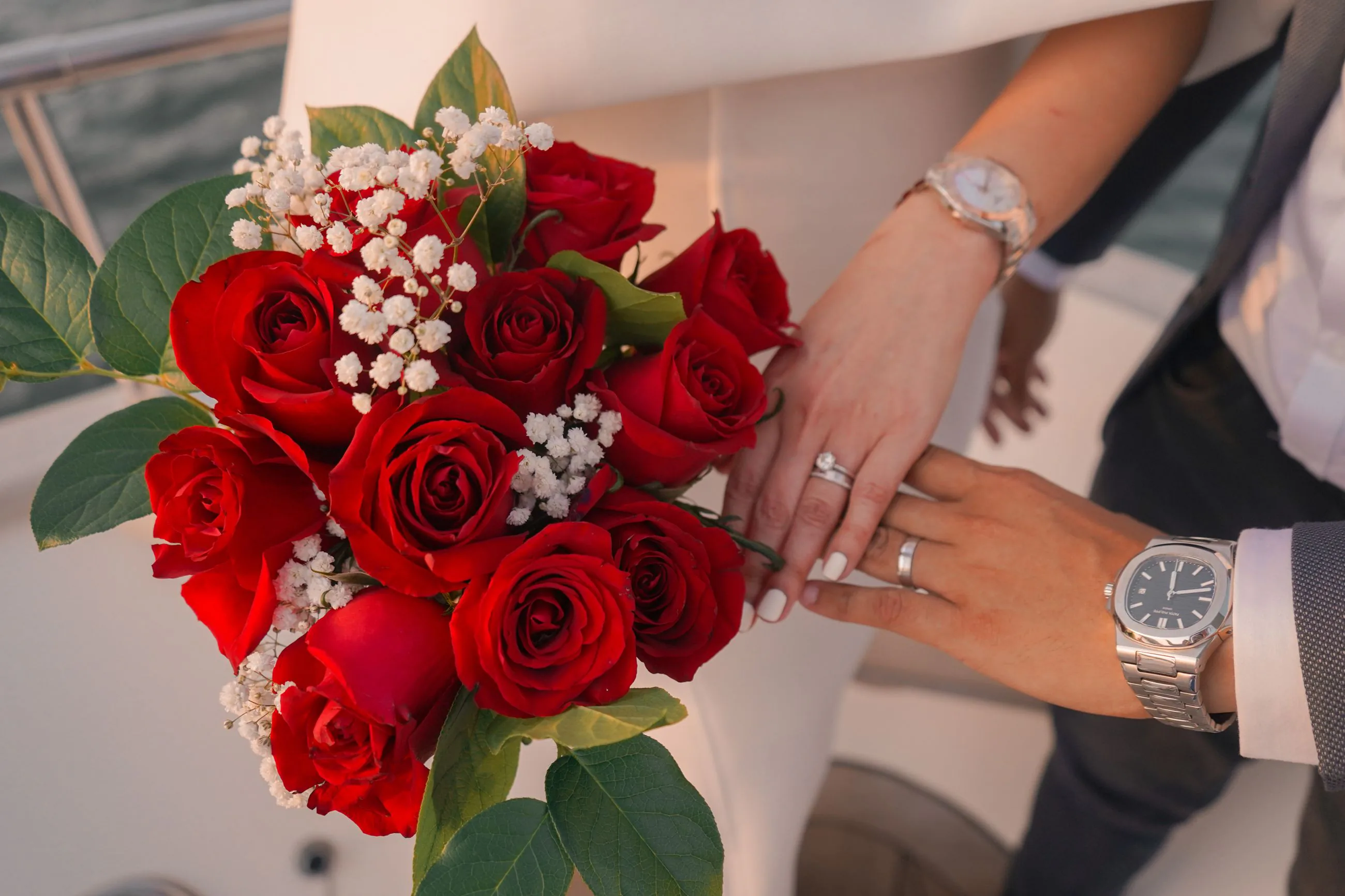 Un bouquet de roses rouges à côté des mains des mariés et de leurs alliances